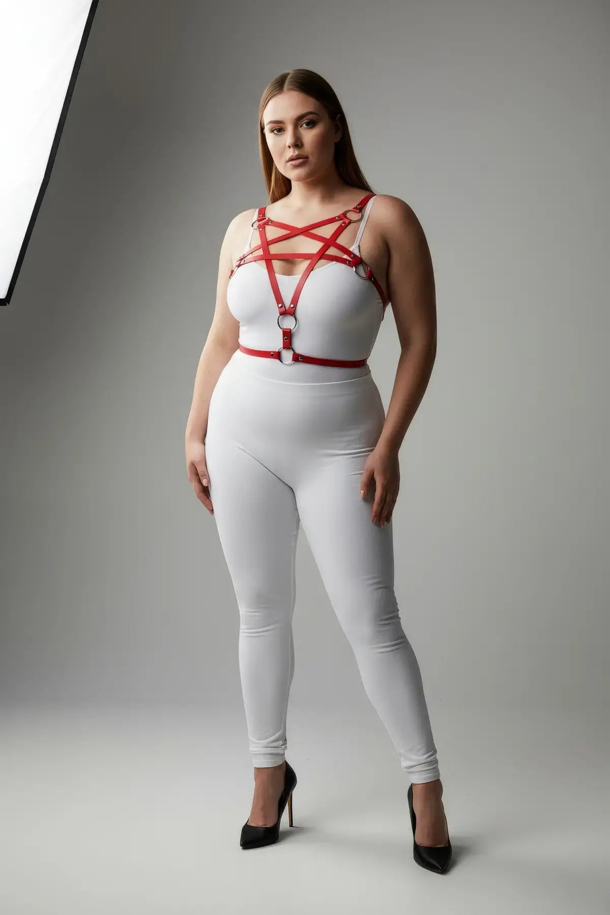 Plus-size red faux-leather O-ring harness with four rings and crisscross straps over a white outfit