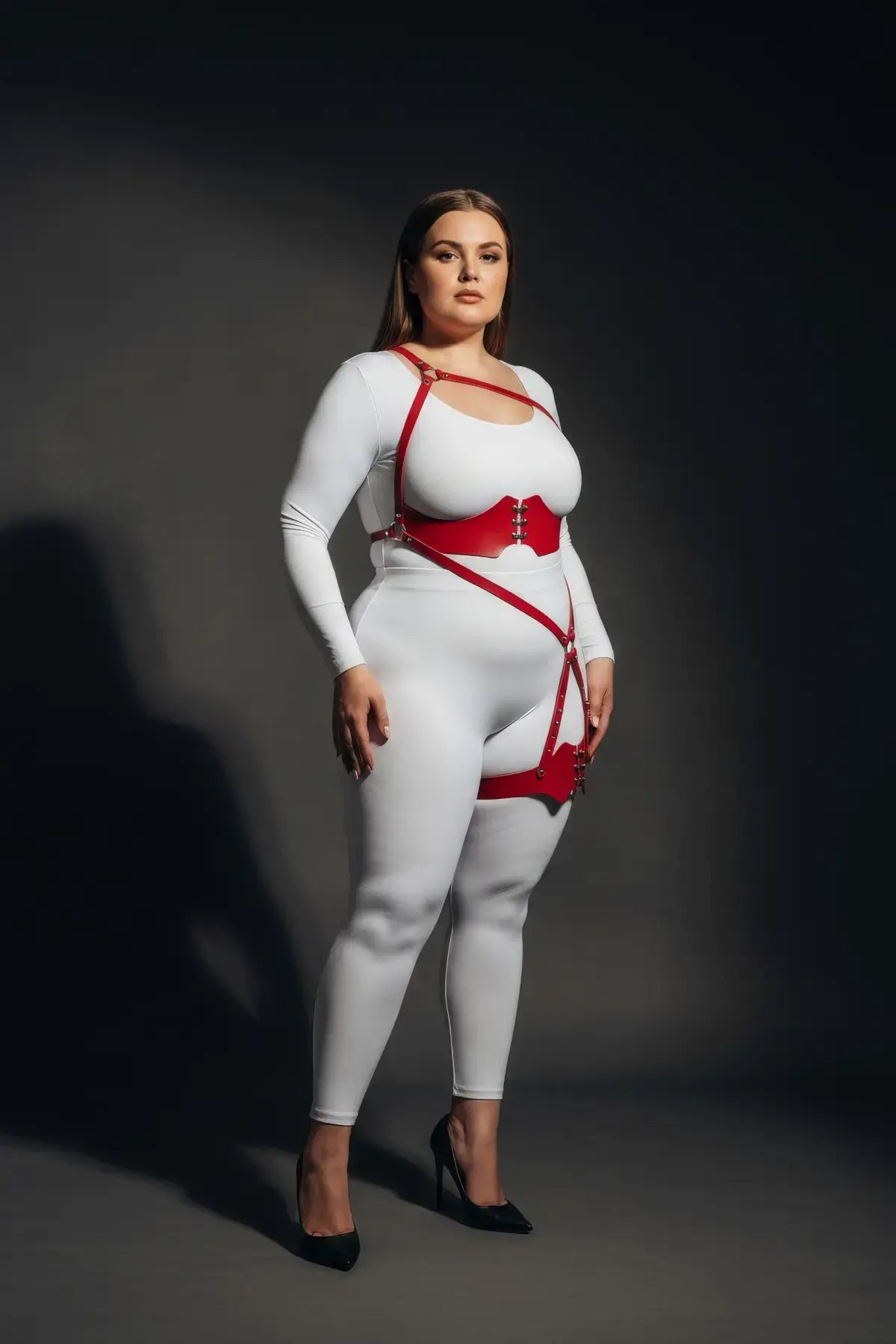 Plus-size red one-shoulder bustier harness with scalloped thigh garter in vegan leather, shown on a model.