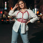 Plus-size red vegan-leather shoulder-strap corset harness worn over a white shirt.