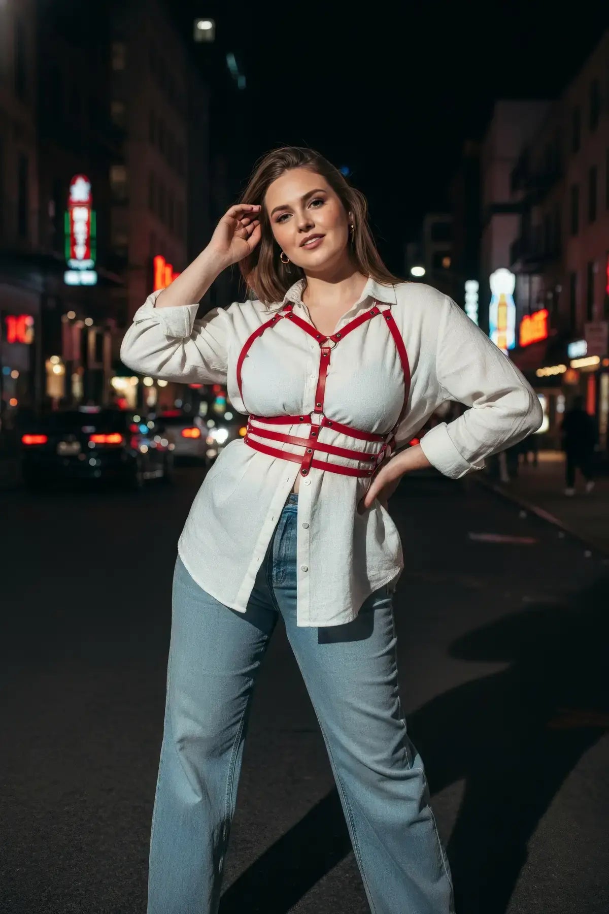 Plus-size red vegan-leather shoulder-strap corset harness worn over a white shirt.