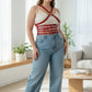 Plus-size HarnessClub red leather shoulder-strap corset harness worn over a white top and jeans.