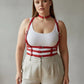 Plus size red strappy body harness with vegan leather choker and multiple buckles worn over a white tank top.