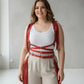 Plus-size red tassel-detail leather body harness with multiple straps and long fringe worn over a white ribbed tank top.