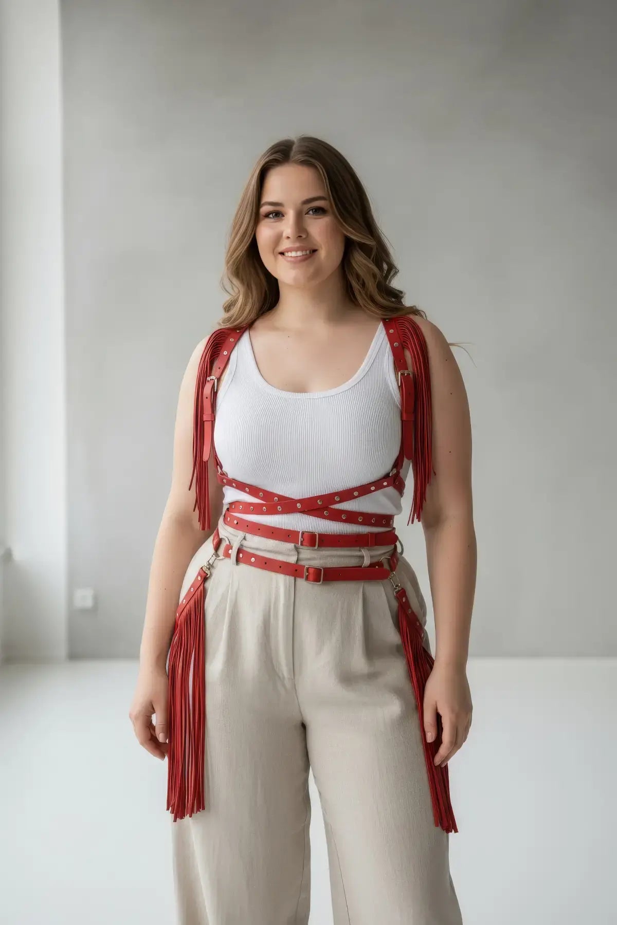 Plus-size red tassel-detail leather body harness with multiple straps and long fringe worn over a white ribbed tank top.