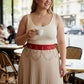 Plus-size red vegan leather waist belt with twin silver O-rings and chain detailing worn over a beige pleated skirt
