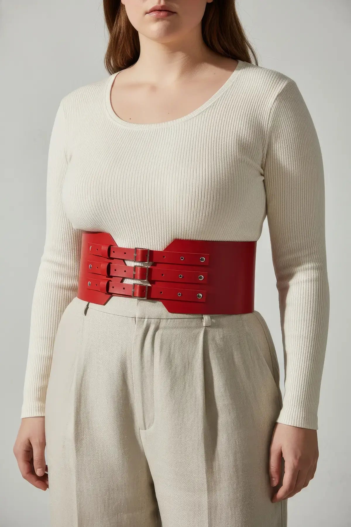 Plus size red vegan leather wide-buckle corset belt with triple buckles worn over a beige outfit for waist cinching