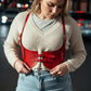 Plus-size red vegan-leather under-bust corset belt harness with dual buckles worn over a cream sweater