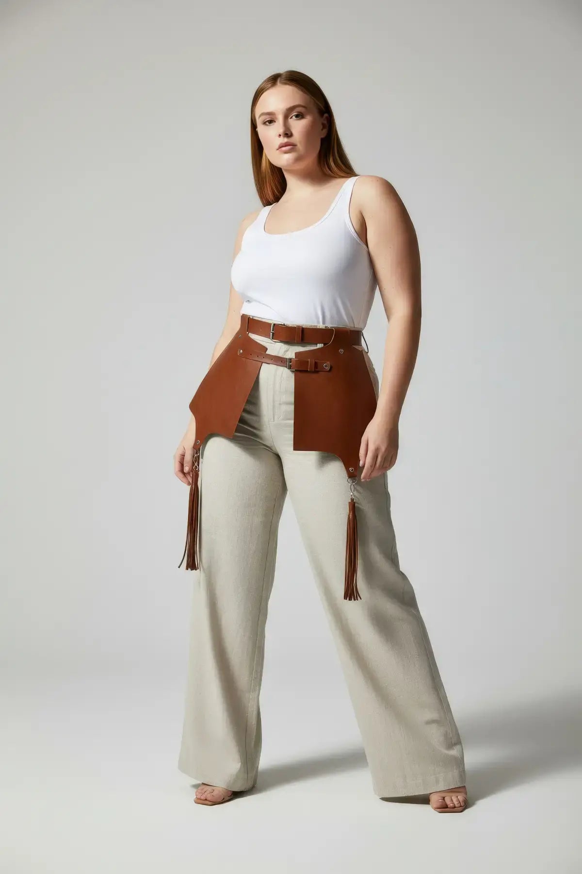 Plus Size tan leather corset harness with tassel detail, shown on model over a white tank top.