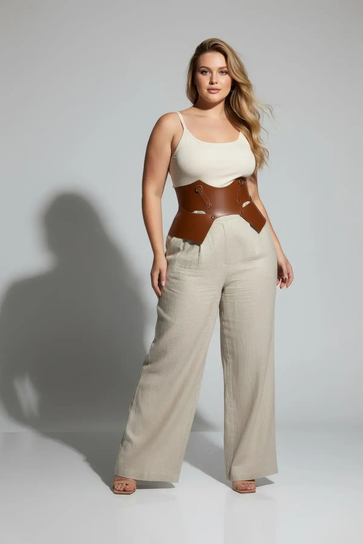 Plus-size tan vegan leather lace-up corset belt around the waist on a model wearing a cream top and beige wide-leg pants