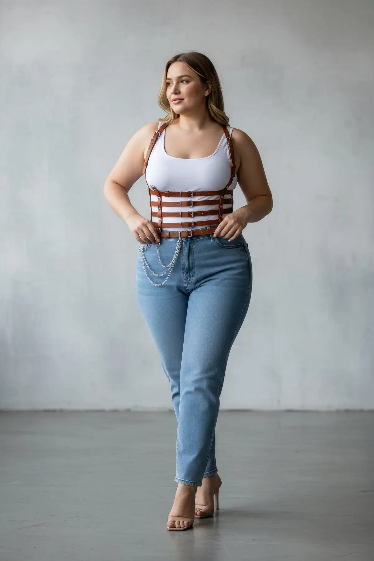Plus-size tan vegan-leather multi-strap suspender corset harness with chain detail, worn over a tank top and jeans