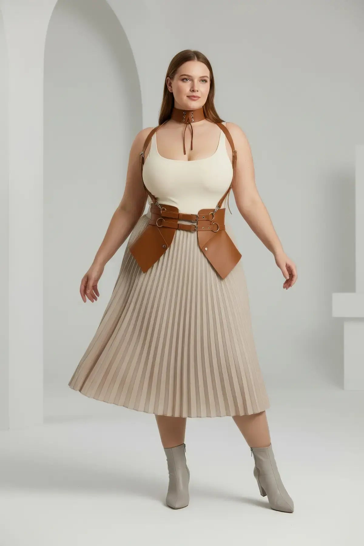 Plus-size tan vegan leather suspender corset harness with choker and hip flaps, worn over a cream top and beige pleated skirt.
