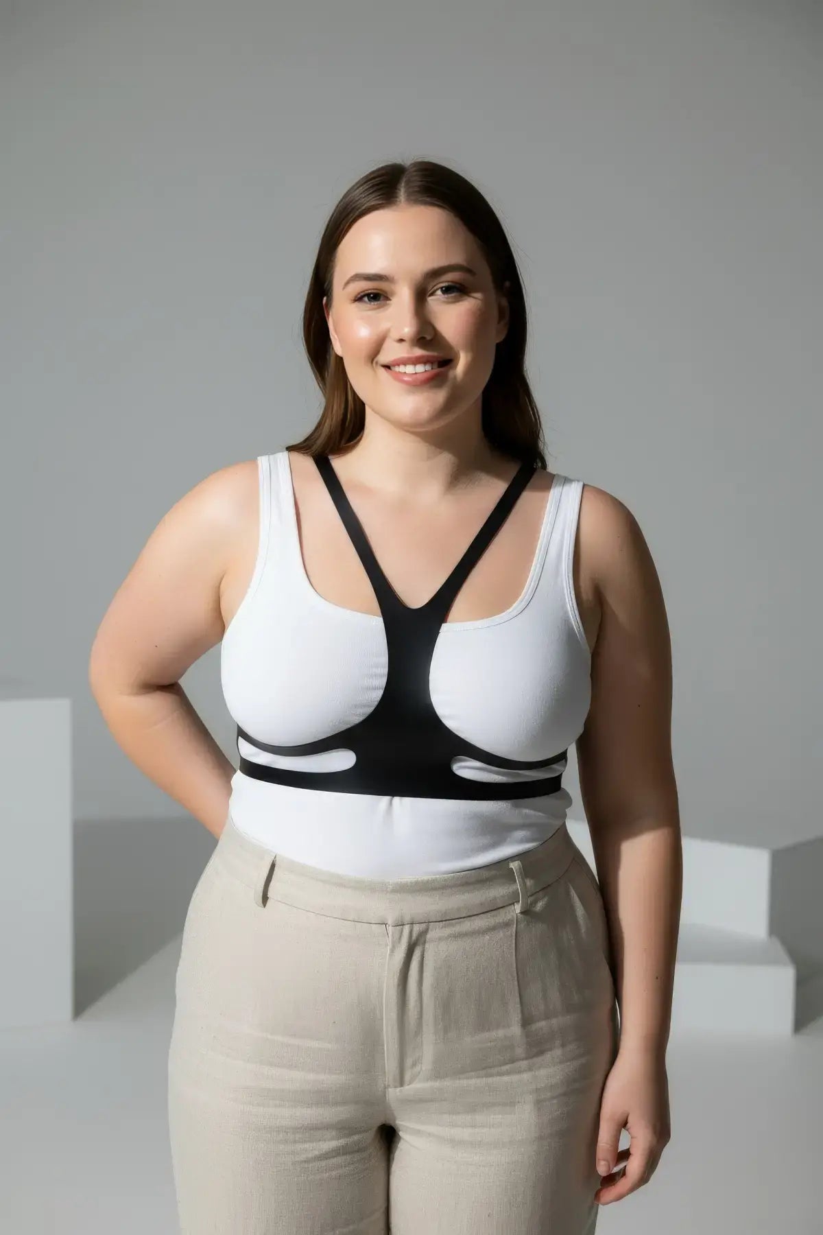 Plus-size vegan leather body harness belt in black worn over a white tank top for festival and clubwear.