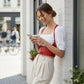 Red lace-up underbust corset belt with straps in vegan leather, worn over a white blouse by a woman outdoors