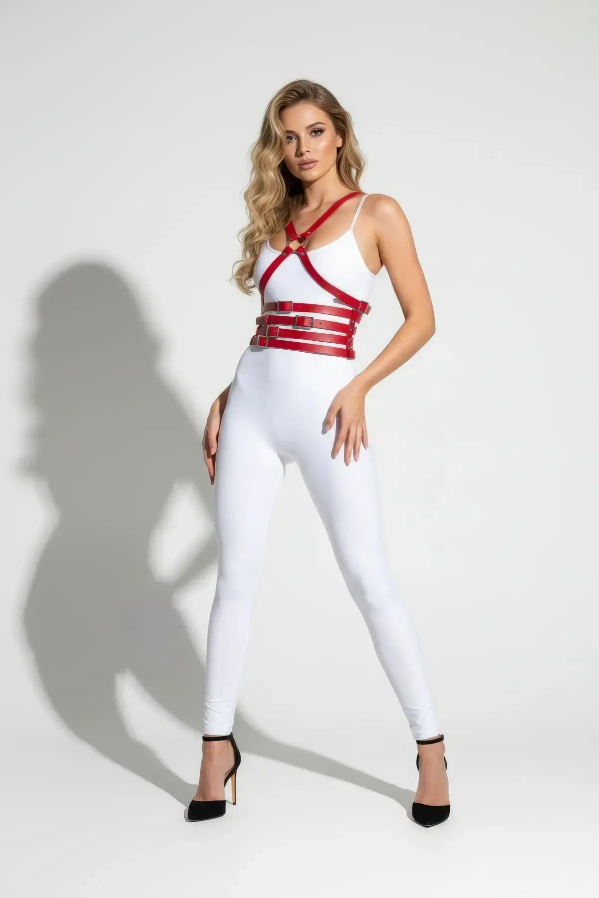 Red multi-band body harness by HarnessClub worn over a white bodysuit; vegan leather chest and waist accessory.