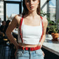 Red shoulder-strap waist harness, vegan leather, worn over a white crop top.