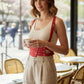 Red studded waist-panel vegan leather harness worn over a white ribbed tank top