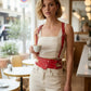 Red vegan-leather studded waist-panel harness worn over a white top in a cafe.