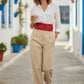 Red wide corset belt in vegan leather with double buckles worn at the waist over a white blouse and beige trousers
