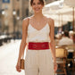 Red wide corset belt in vegan leather by HarnessClub, worn at the waist over a white top.