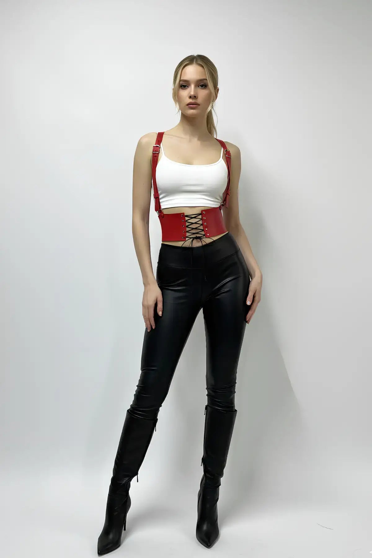 Red vegan-leather corset waist belt with lace-up and suspenders worn by model in a white crop top and black pants