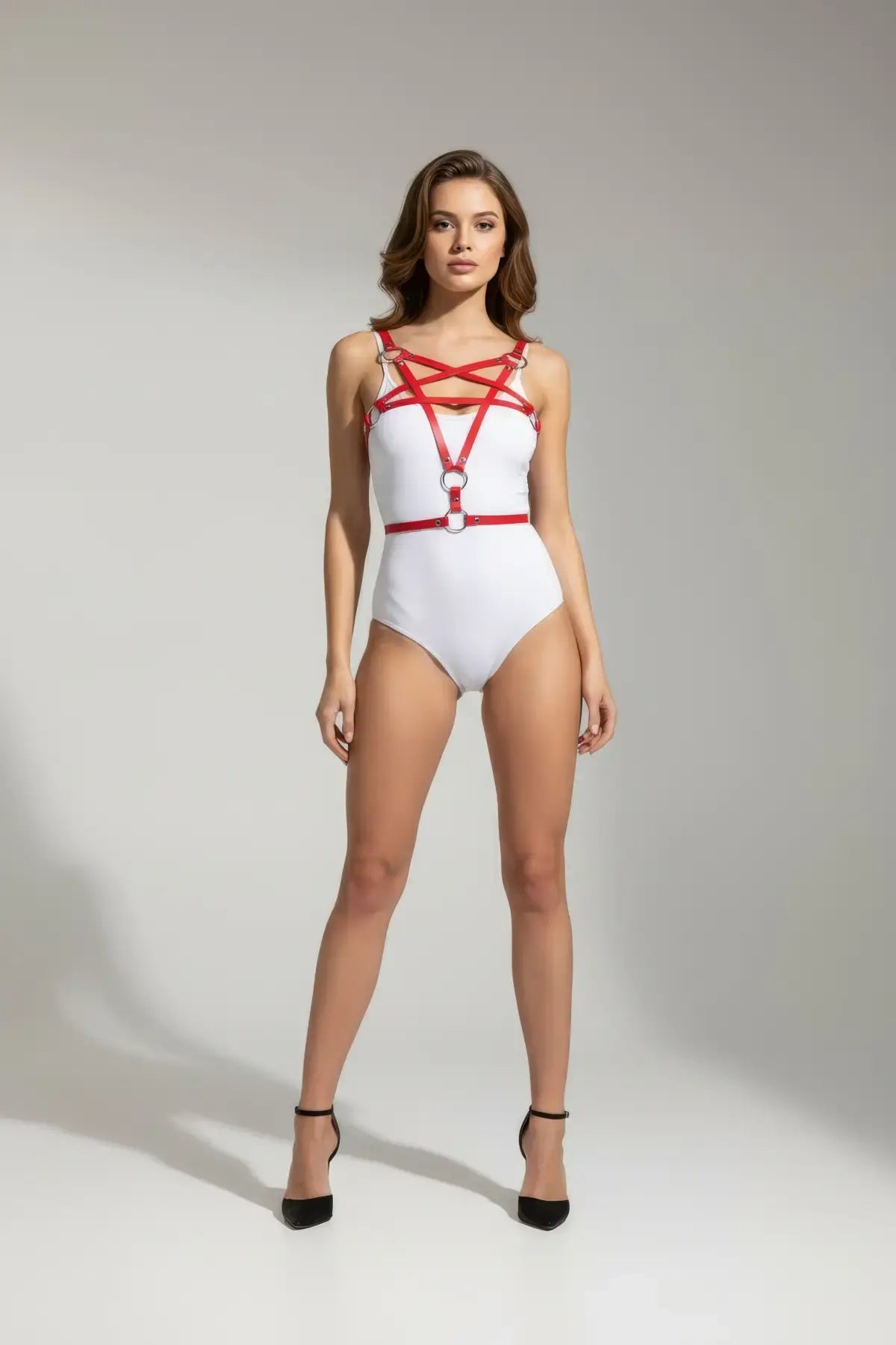 Red star-cross chest and underbust vegan leather harness worn over a white bodysuit.