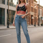 Women's red chain and stud strap body harness worn over a black crop top and blue jeans.