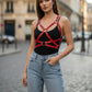 Women's red vegan leather crossbody body harness over black top, paired with blue jeans.