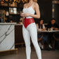 Womens red studded corset belt worn at the waist over a white bodysuit; vegan leather waist accessory.